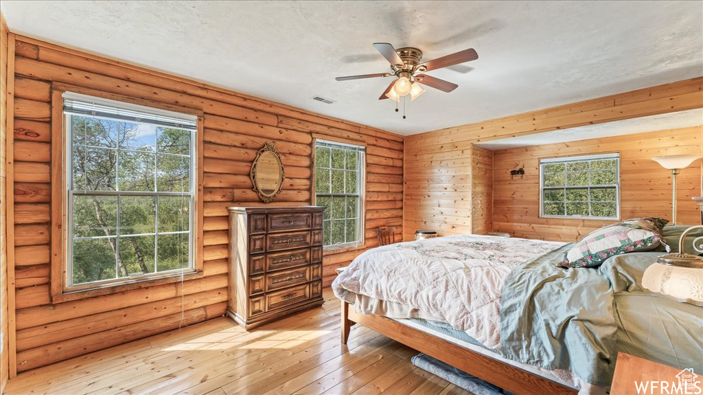 Bedroom with light hardwood / wood-style flooring, ceiling fan, and rustic walls