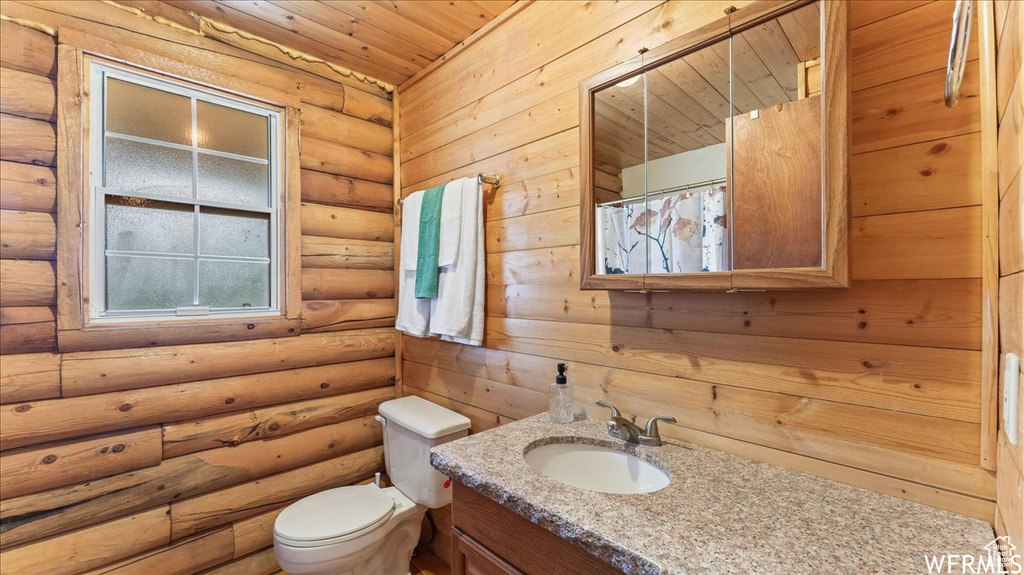 Bathroom featuring rustic walls, toilet, vanity, and wood ceiling