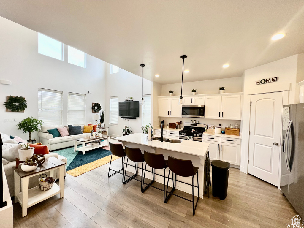 Kitchen with appliances with stainless steel finishes, white cabinetry, light hardwood / wood-style flooring, and pendant lighting
