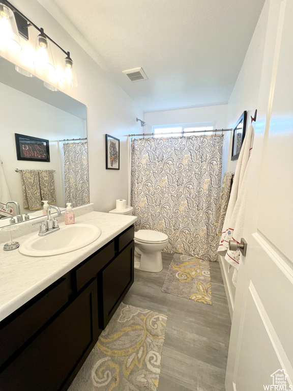 Full bathroom with hardwood / wood-style floors, toilet, shower / tub combo, and vanity with extensive cabinet space