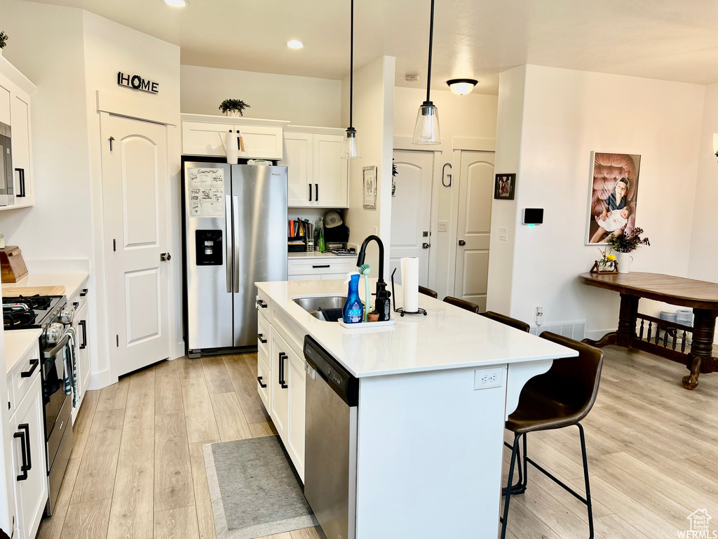 Kitchen with decorative light fixtures, white cabinetry, appliances with stainless steel finishes, and light hardwood / wood-style floors