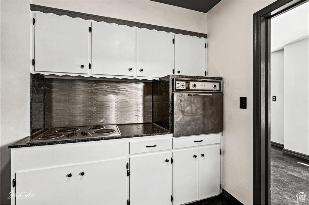 Kitchen featuring white cabinets, backsplash, dark tile flooring, and stainless steel gas cooktop