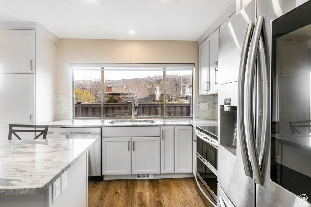 Kitchen with stainless steel appliances, tasteful backsplash, light hardwood / wood-style flooring, sink, and light stone counters