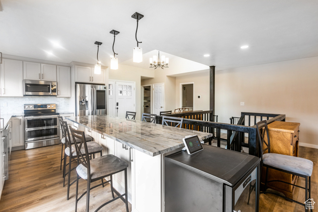 Kitchen with decorative light fixtures, backsplash, a notable chandelier, appliances with stainless steel finishes, and light hardwood / wood-style floors