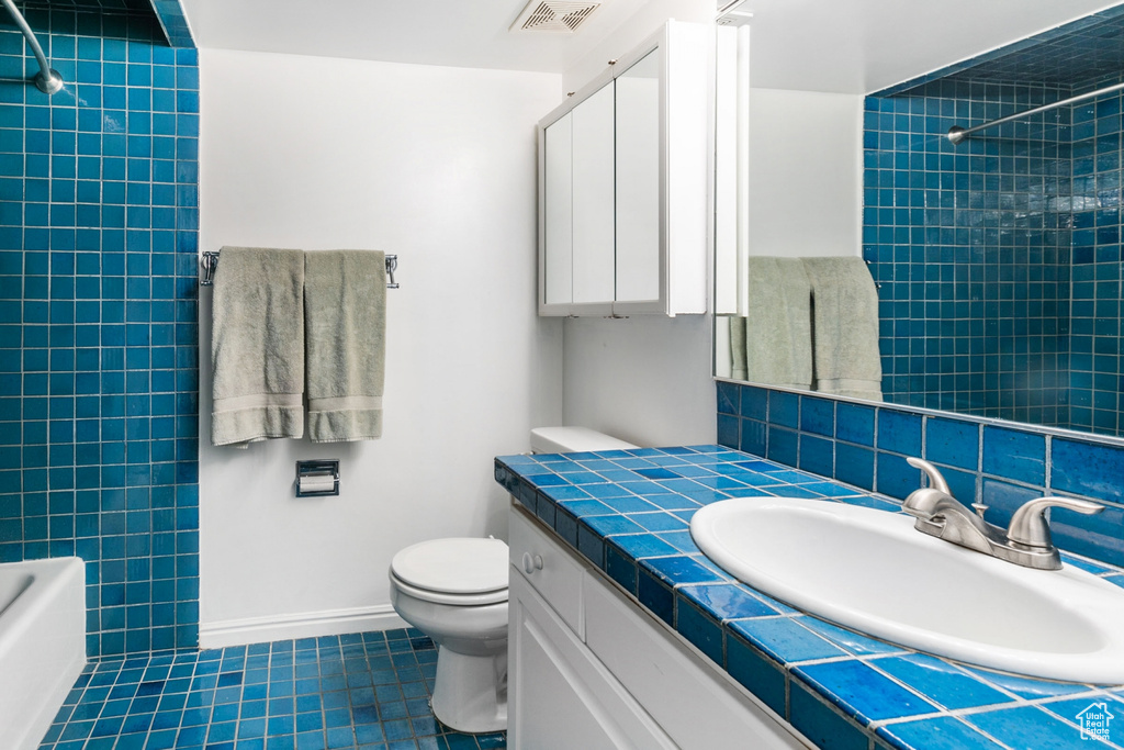 Full bathroom featuring tiled shower / bath combo, tile floors, oversized vanity, and toilet