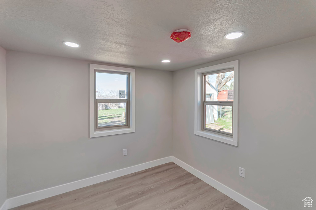 Empty room with a textured ceiling and light hardwood / wood-style flooring