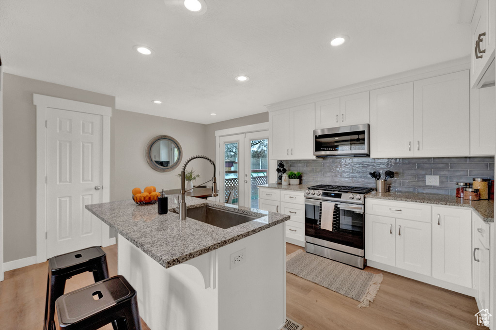 Kitchen featuring a breakfast bar, stainless steel appliances, white cabinetry, light stone countertops, and french doors