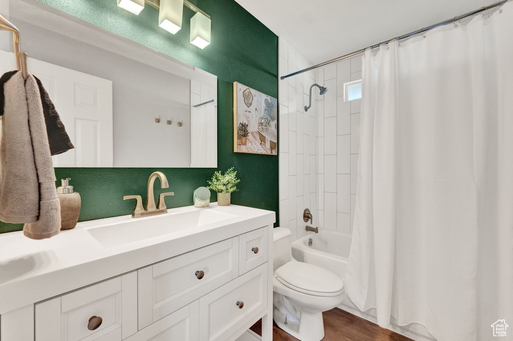 Full bathroom with toilet, vanity, shower / bathtub combination with curtain, and hardwood / wood-style flooring