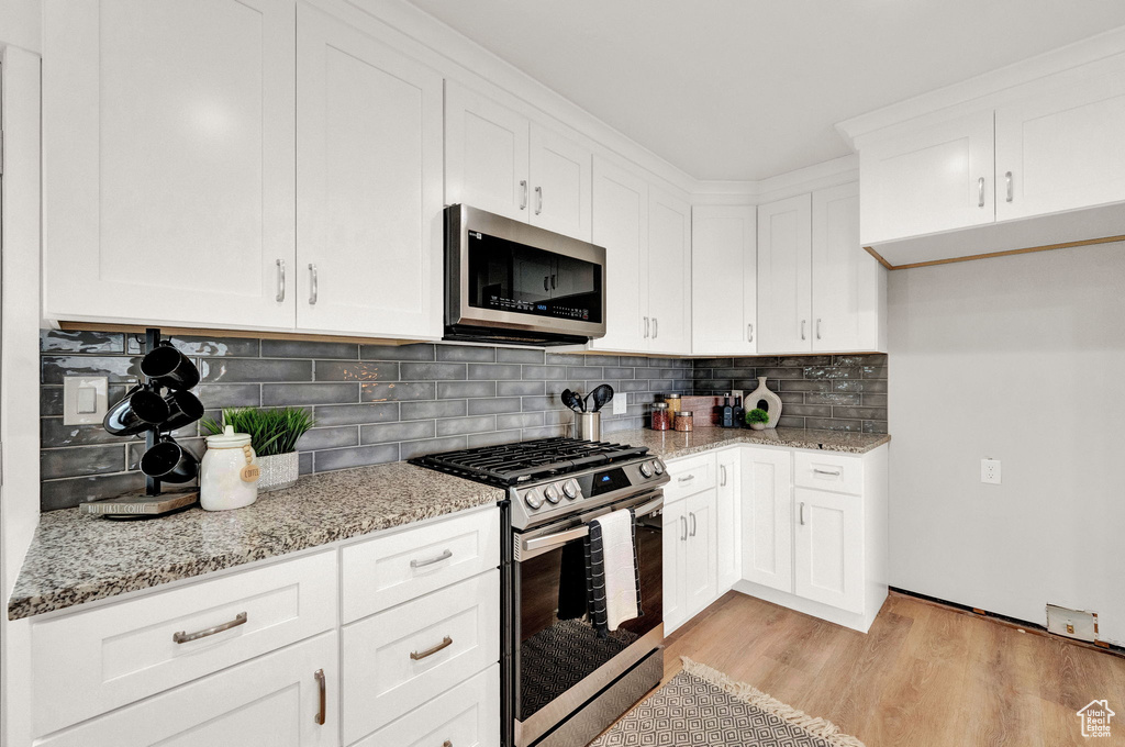 Kitchen with white cabinets, light hardwood / wood-style floors, light stone counters, and stainless steel appliances