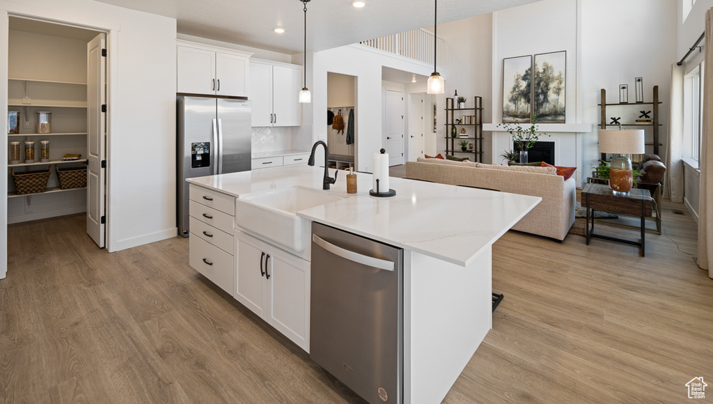 Kitchen with appliances with stainless steel finishes, pendant lighting, a center island with sink, and light hardwood / wood-style floors