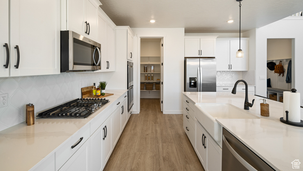 Kitchen featuring appliances with stainless steel finishes, hanging light fixtures, tasteful backsplash, light hardwood / wood-style floors, and white cabinets