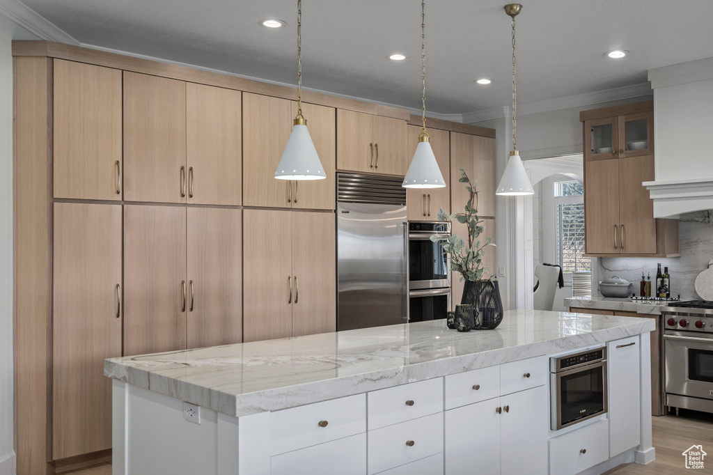 Kitchen with white cabinets, decorative light fixtures, light stone counters, and high end appliances
