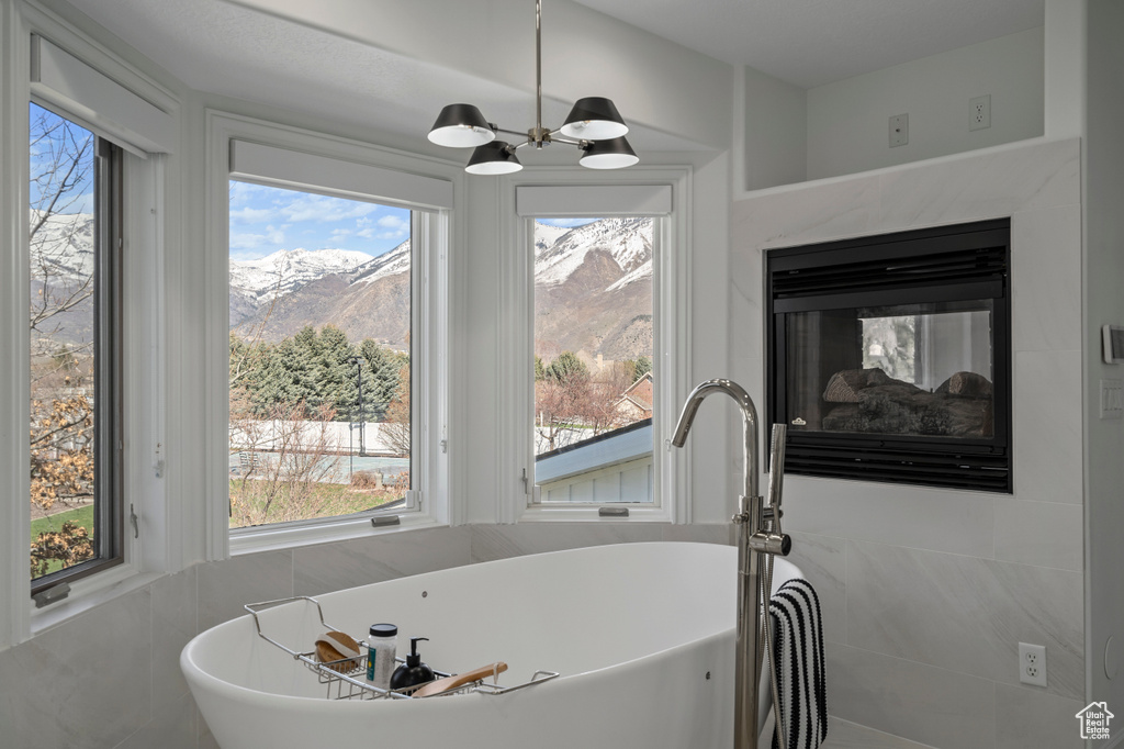 Bathroom featuring tile walls, a bath to relax in, a mountain view, and an inviting chandelier