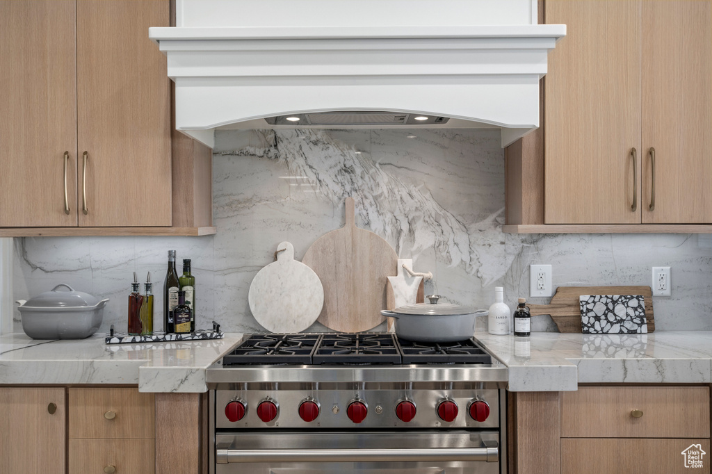 Kitchen featuring light stone countertops, high end stove, tasteful backsplash, and premium range hood