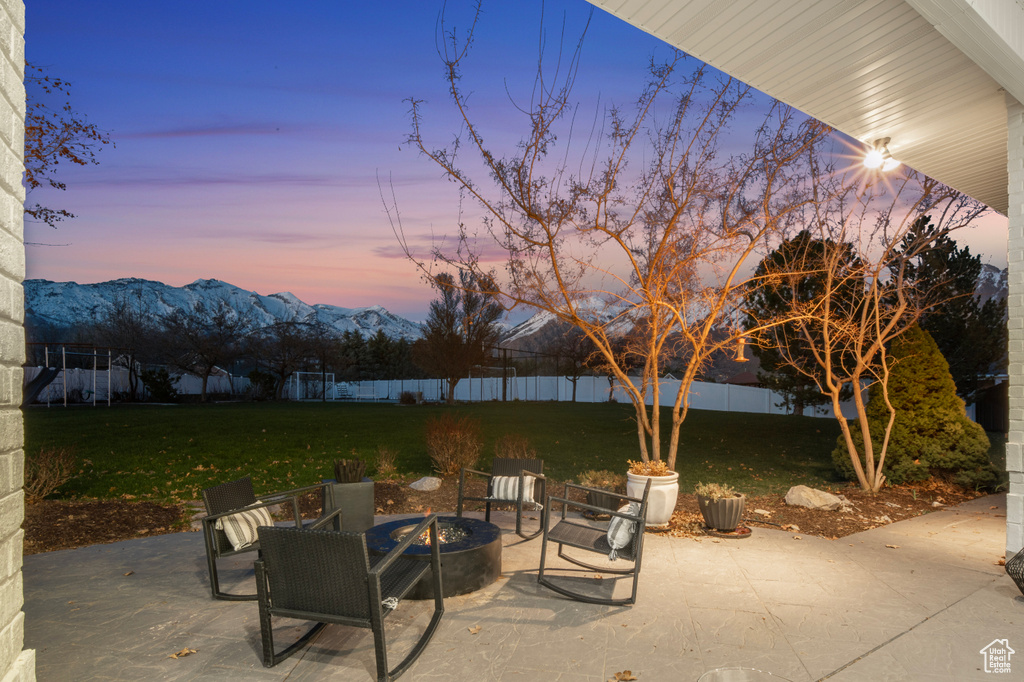 Patio terrace at dusk featuring a lawn, a mountain view, and an outdoor fire pit