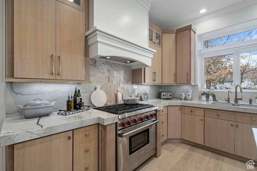Kitchen featuring light stone countertops, backsplash, premium range, sink, and light hardwood / wood-style flooring