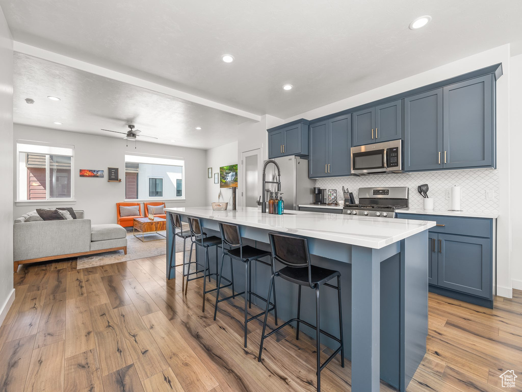 Kitchen featuring ceiling fan, a kitchen breakfast bar, appliances with stainless steel finishes, light hardwood / wood-style flooring, and backsplash