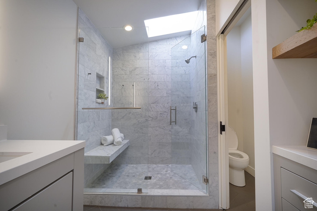 Bathroom featuring lofted ceiling with skylight, vanity, tile floors, a shower with shower door, and toilet