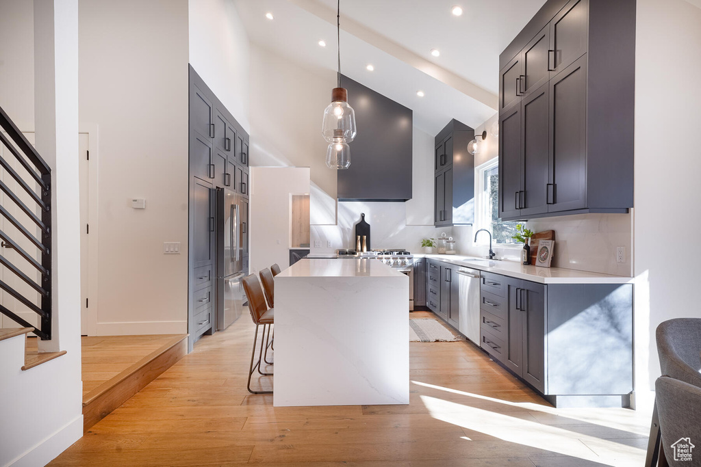 Kitchen with a center island, light hardwood / wood-style floors, backsplash, dishwasher, and decorative light fixtures