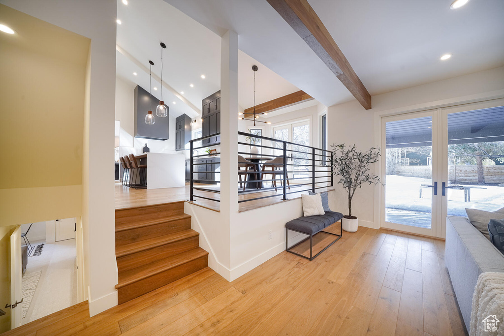 Staircase with lofted ceiling with beams, plenty of natural light, an inviting chandelier, and light hardwood / wood-style floors