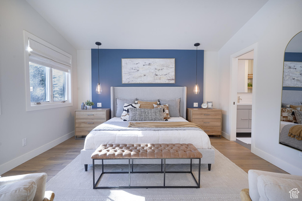 Bedroom with vaulted ceiling, ensuite bath, and hardwood / wood-style floors