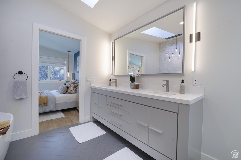 Bathroom featuring hardwood / wood-style floors, double vanity, and vaulted ceiling with skylight