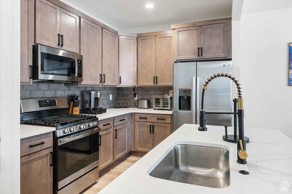 Kitchen with tasteful backsplash, appliances with stainless steel finishes, and light hardwood / wood-style flooring