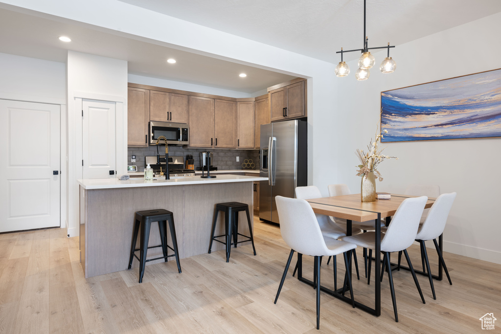 Kitchen featuring backsplash, light hardwood / wood-style floors, stainless steel appliances, a center island with sink, and a breakfast bar area