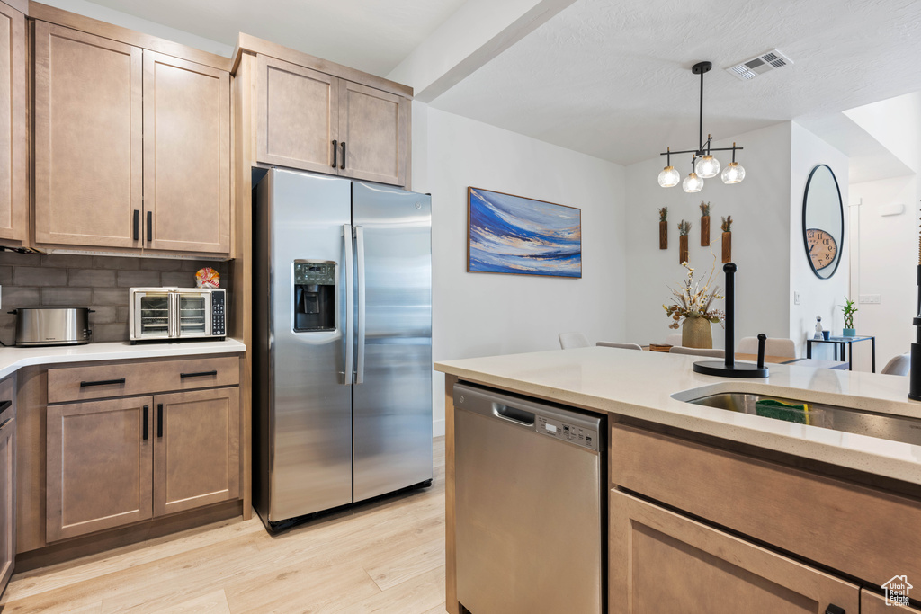Kitchen with hanging light fixtures, a notable chandelier, appliances with stainless steel finishes, light hardwood / wood-style floors, and tasteful backsplash