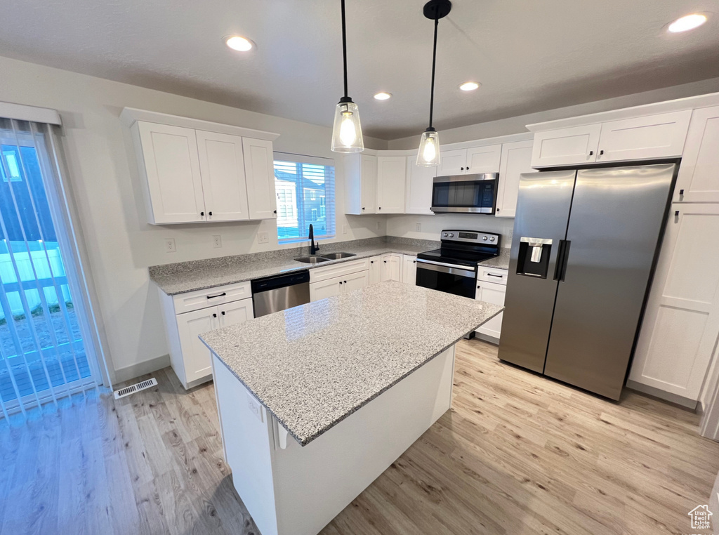 Kitchen featuring pendant lighting, white cabinets, light hardwood / wood-style flooring, stainless steel appliances, and a center island