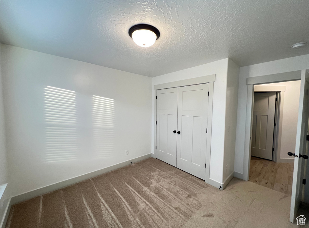 Unfurnished bedroom featuring a closet, a textured ceiling, and light colored carpet