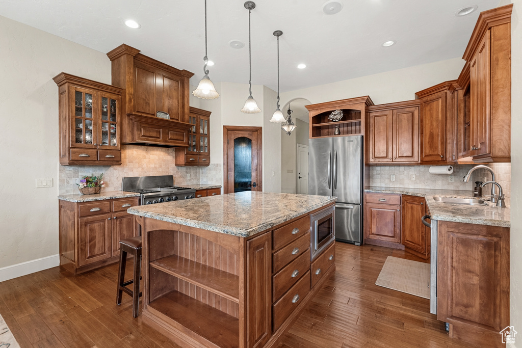 Kitchen with hanging light fixtures, backsplash, stainless steel appliances, dark wood-type flooring, and a center island