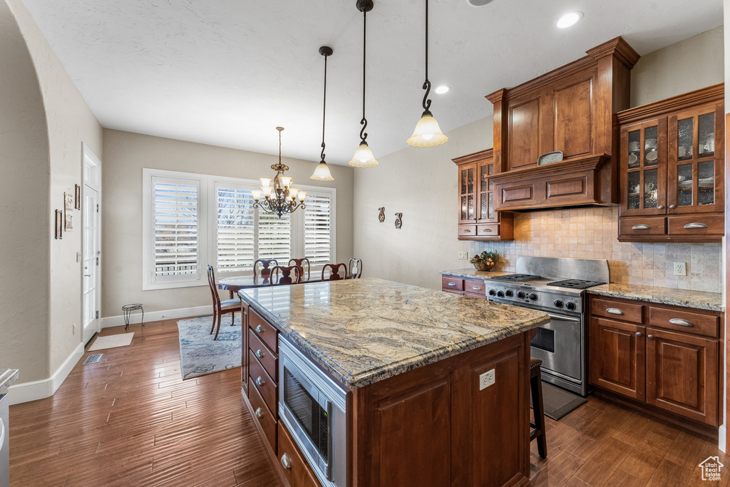 Kitchen with a kitchen island, appliances with stainless steel finishes, backsplash, light stone countertops, and a notable chandelier