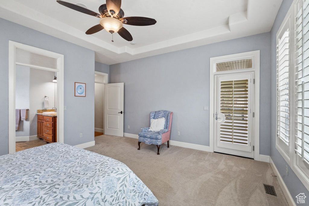 Carpeted bedroom featuring ceiling fan, multiple windows, and a tray ceiling