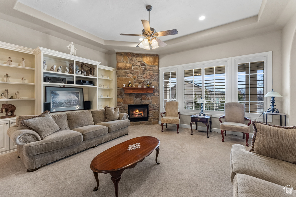 Living room featuring ceiling fan, light colored carpet, a stone fireplace, and a tray ceiling