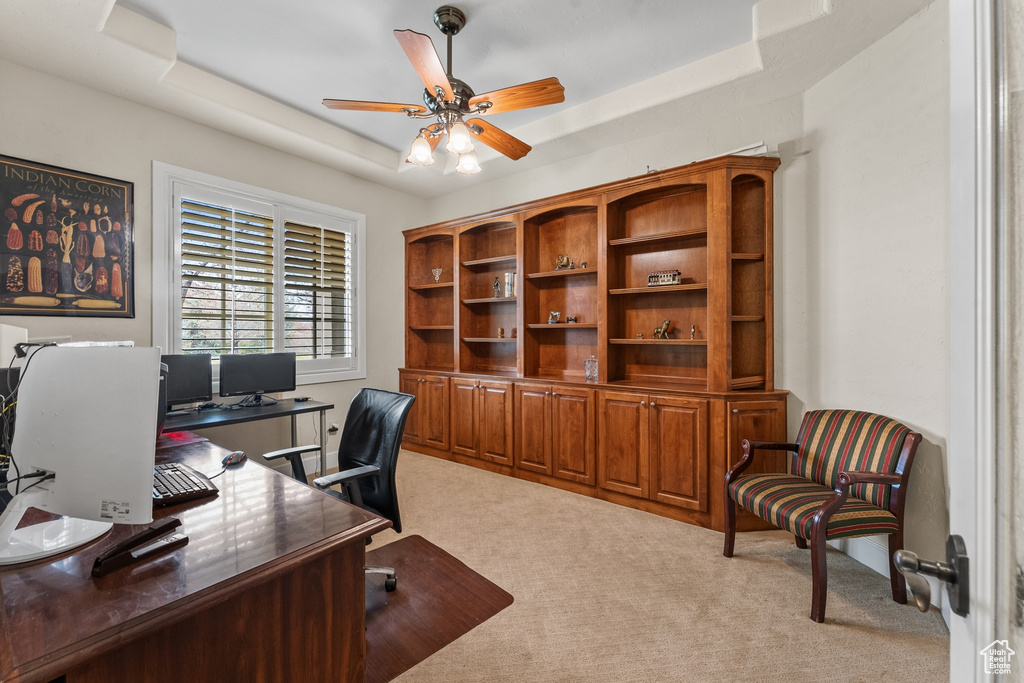 Carpeted office featuring ceiling fan and a tray ceiling