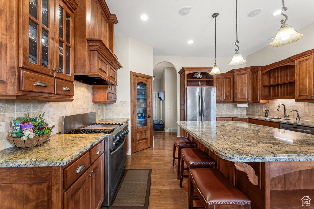 Kitchen with decorative light fixtures, a kitchen bar, tasteful backsplash, dark wood-type flooring, and appliances with stainless steel finishes