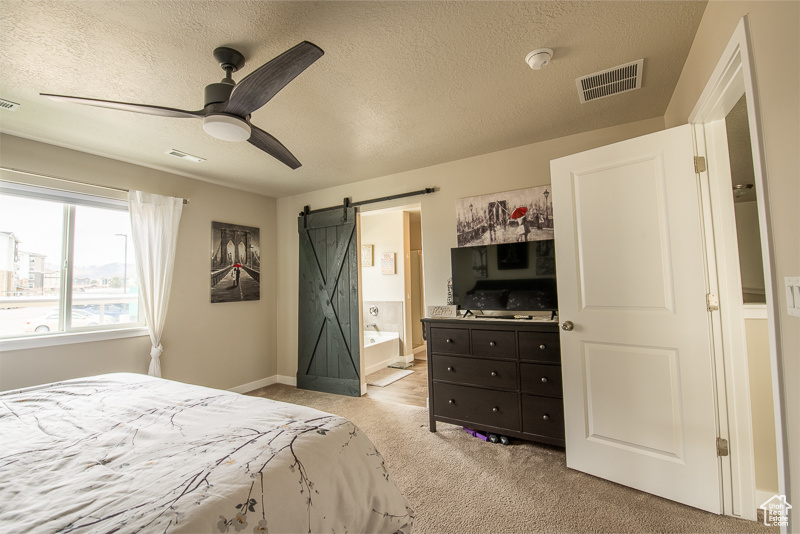 Carpeted bedroom with a barn door, a textured ceiling, ceiling fan, and ensuite bath