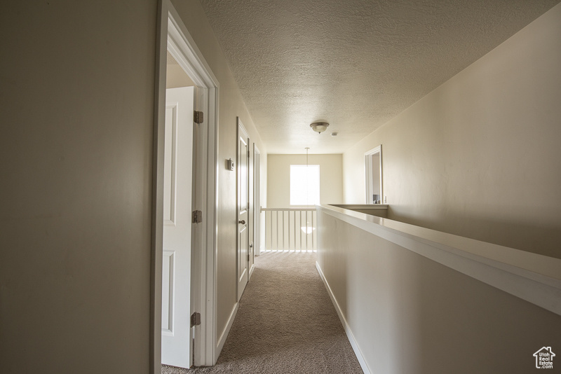 Hallway featuring a textured ceiling and dark carpet