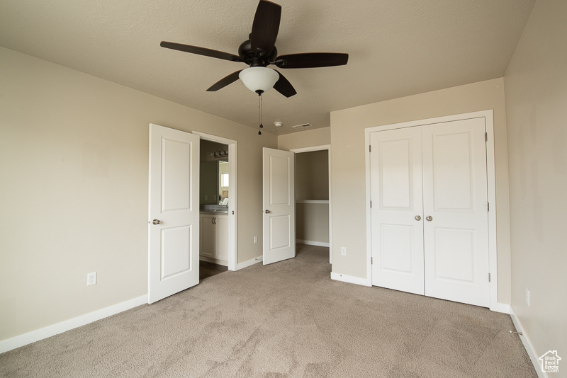 Unfurnished bedroom featuring light carpet, ensuite bathroom, a closet, and ceiling fan