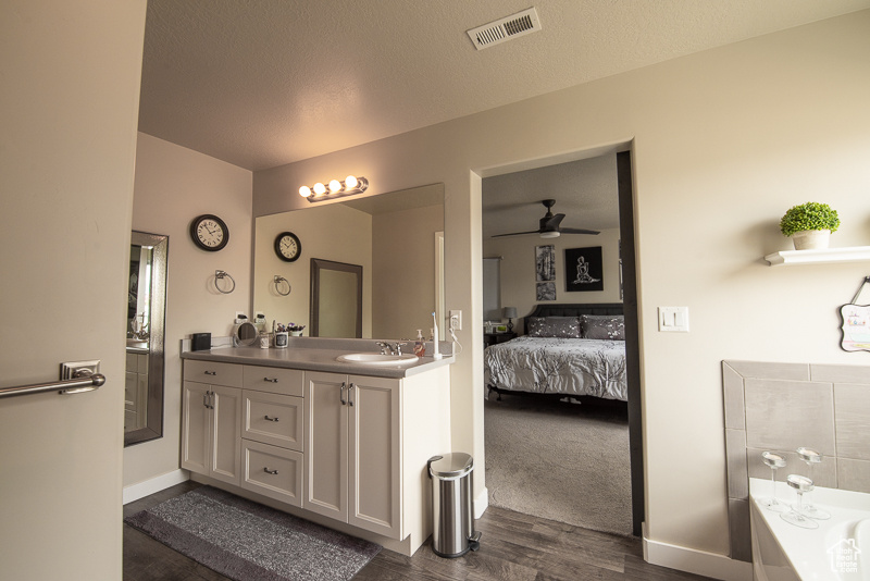 Bathroom with hardwood / wood-style floors, ceiling fan, a washtub, dual sinks, and vanity with extensive cabinet space