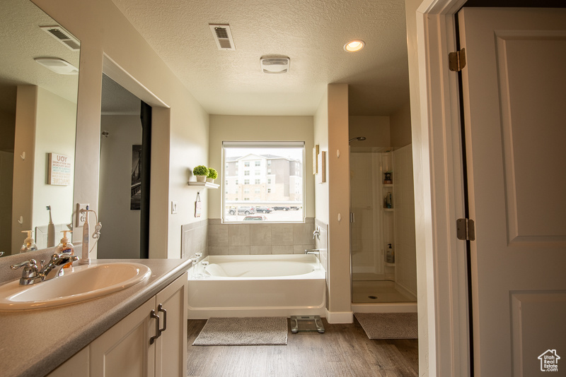 Bathroom featuring independent shower and bath, a textured ceiling, hardwood / wood-style floors, and vanity