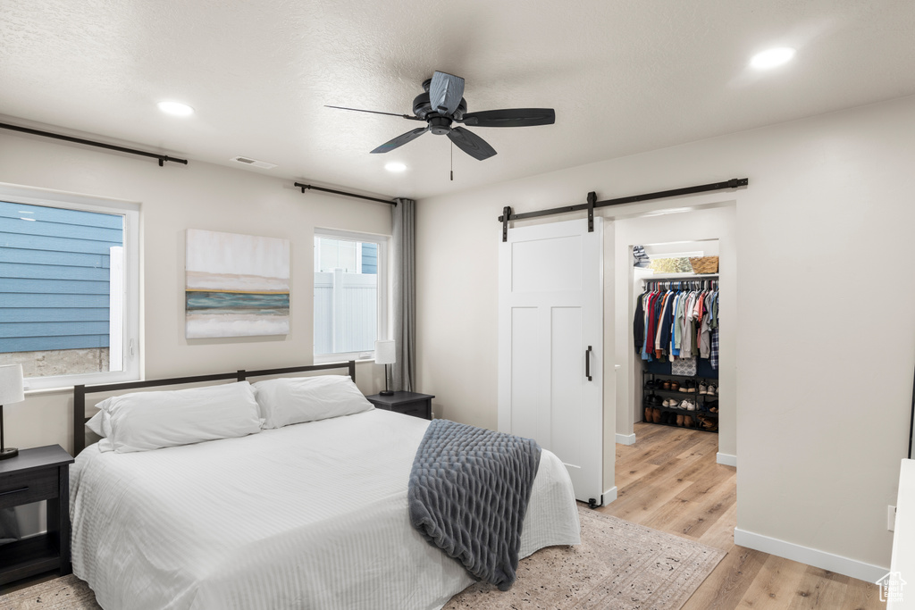 Bedroom featuring a closet, a walk in closet, ceiling fan, a barn door, and light hardwood / wood-style flooring