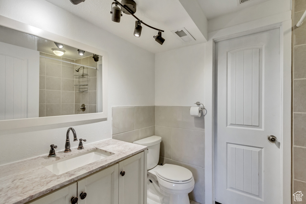 Bathroom with rail lighting, tile walls, toilet, and vanity