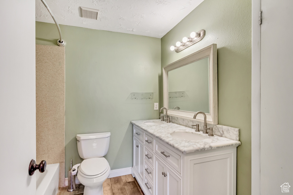 Full bathroom with toilet, double vanity, hardwood / wood-style floors, shower / bathtub combination, and a textured ceiling