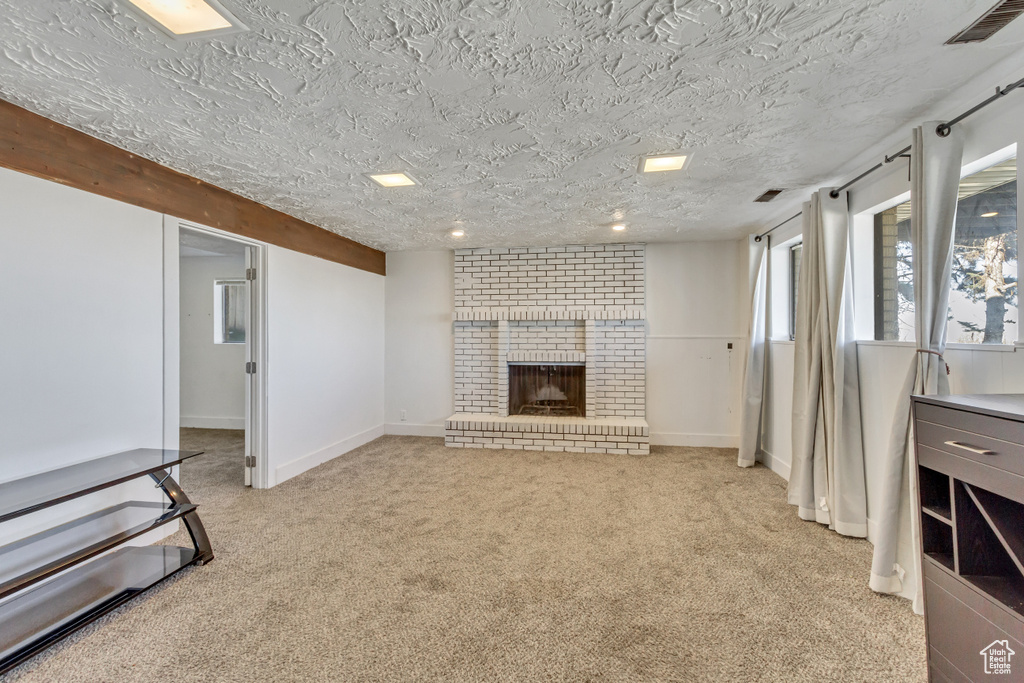Unfurnished living room with brick wall, light carpet, a brick fireplace, and a textured ceiling