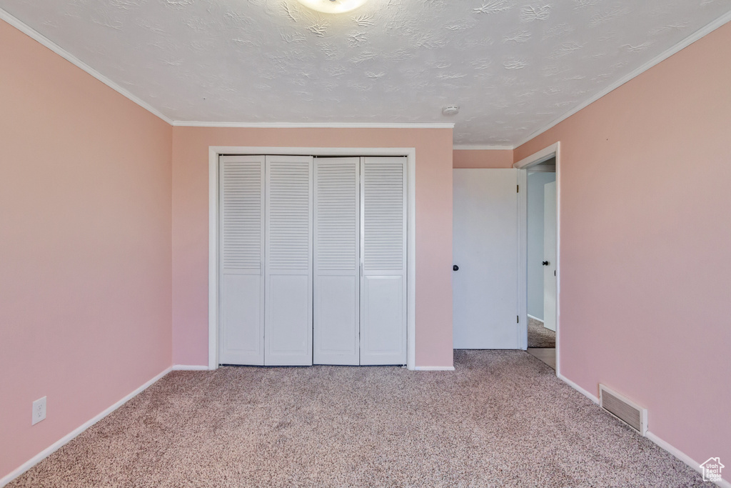 Unfurnished bedroom with light carpet, ornamental molding, a closet, and a textured ceiling