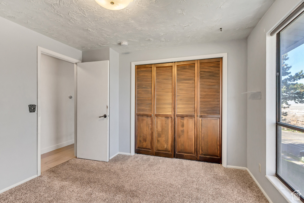 Unfurnished bedroom featuring a textured ceiling, light colored carpet, and a closet