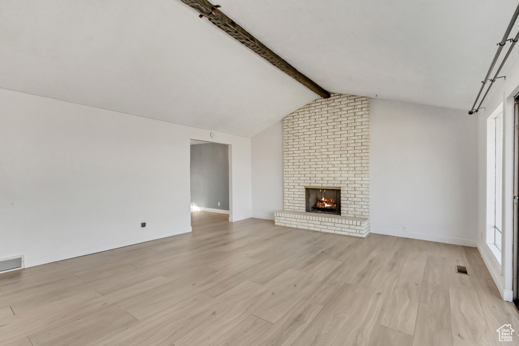 Unfurnished living room with vaulted ceiling with beams, light wood-type flooring, a brick fireplace, and brick wall