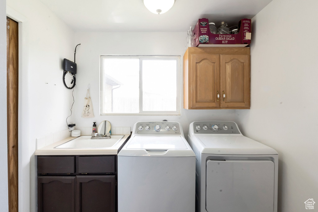 Clothes washing area with cabinets, washer and dryer, and sink